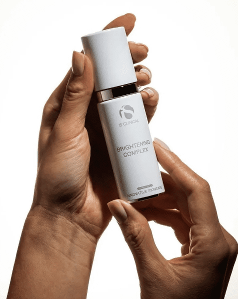 Someone holds a 30g bottle of Brightening Complex against a white background, cradling the skincare product in both hands.